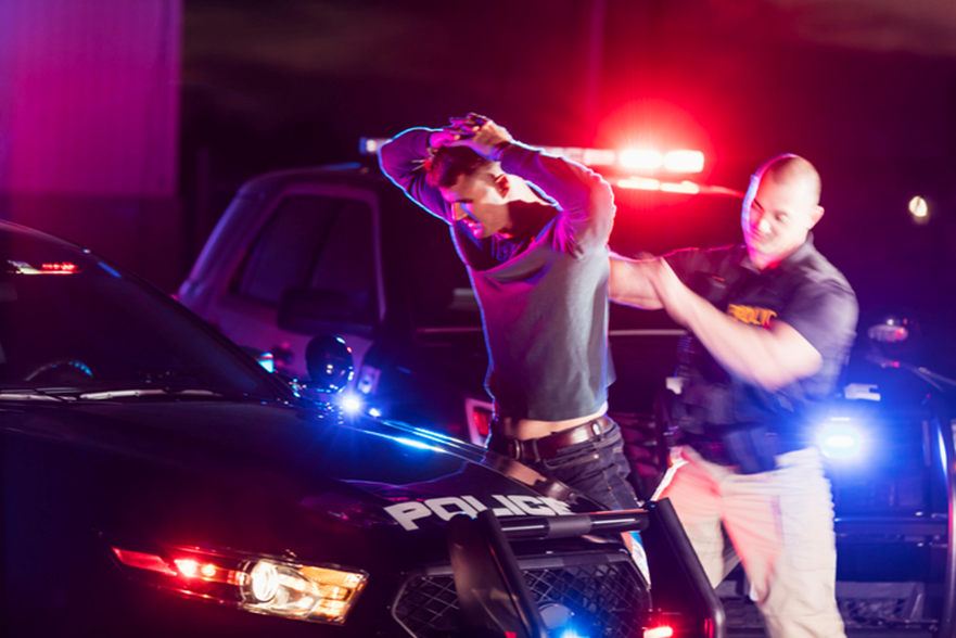 The man is under arrested by a cop and pinned to the cop car